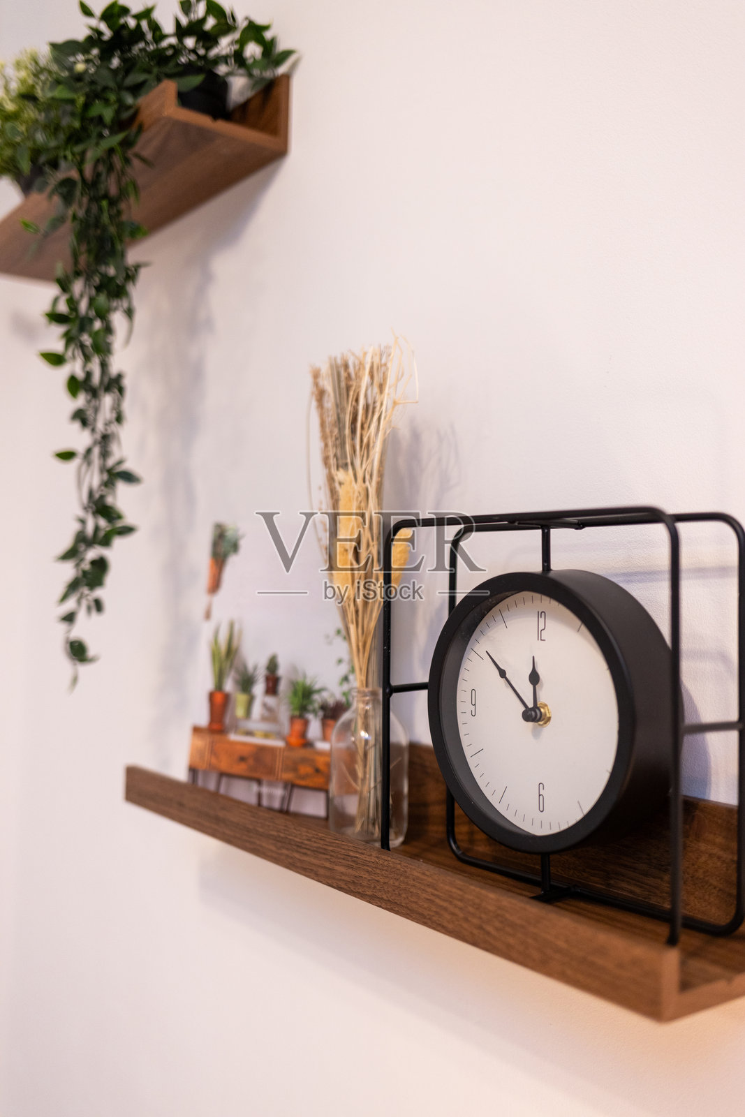 时钟放在白色墙壁上的木架子上。照片摄影图片