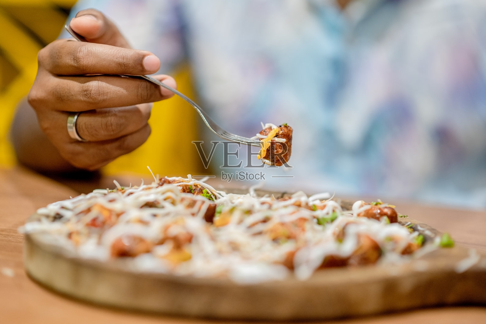 手握叉子和勺子,正在用餐的手放在餐桌上,夹着豆腐沙拉。食物放在桌上的木质托盘里。照片摄影图片