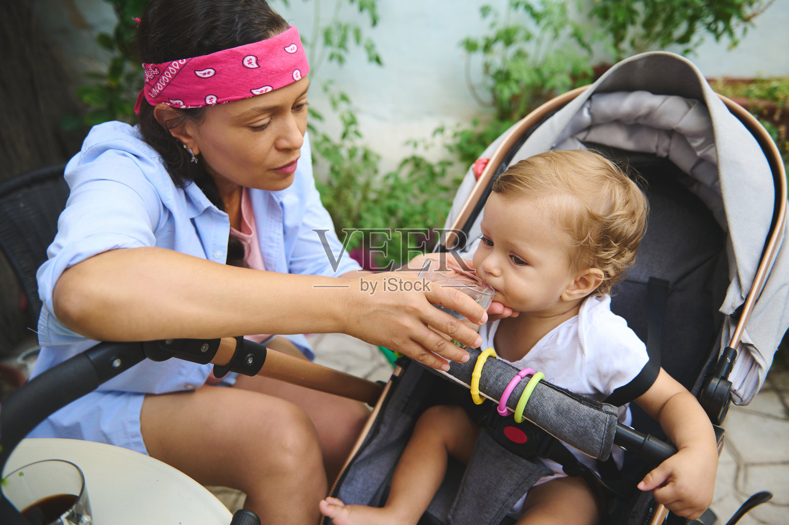 母亲在户外给她的孩子喂饮料,孩子坐在婴儿车里照片摄影图片