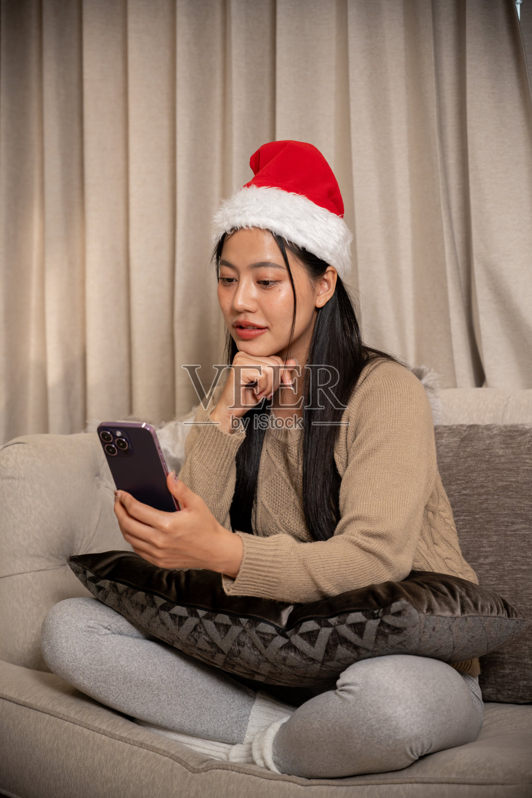 穿着棕色毛衣的亚洲女性在客厅里开心地用手机进行视频通话照片摄影图片