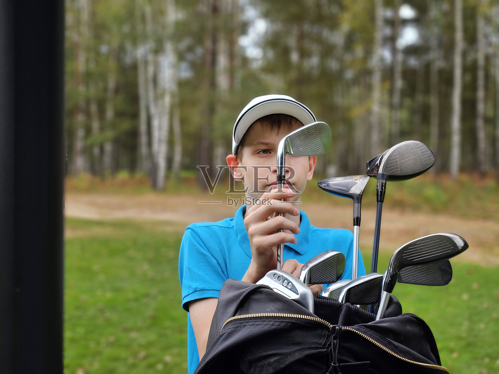 青少年高尔夫球手从球包中选择球杆。照片摄影图片