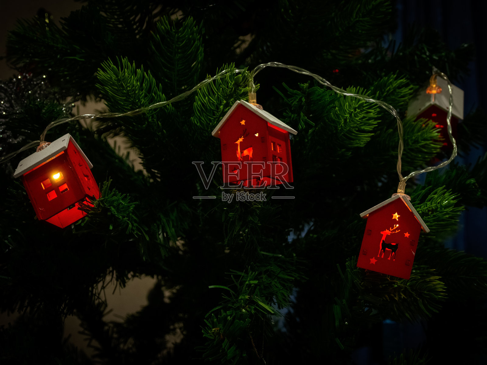 一串房屋形状的圣诞花环,闪烁着树上的灯光,营造出温馨的氛围和神奇的节日气息。照片摄影图片