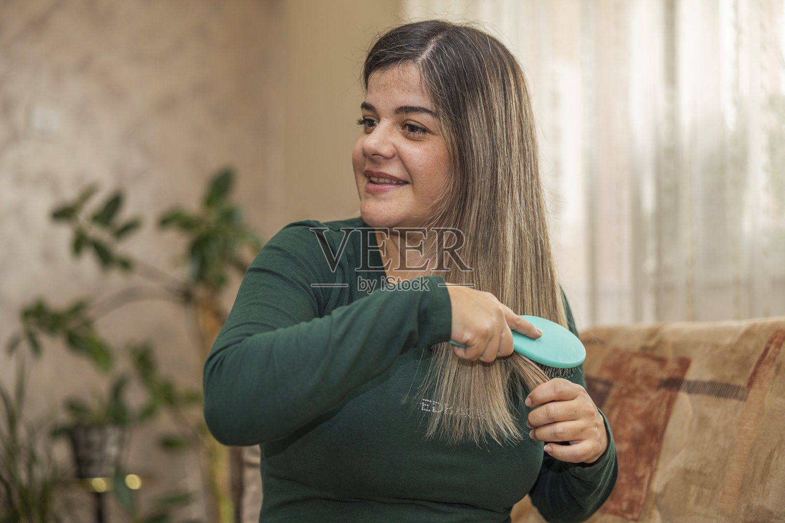 美丽微笑的女性自信地坐在客厅沙发上用梳子梳理头发。照片摄影图片