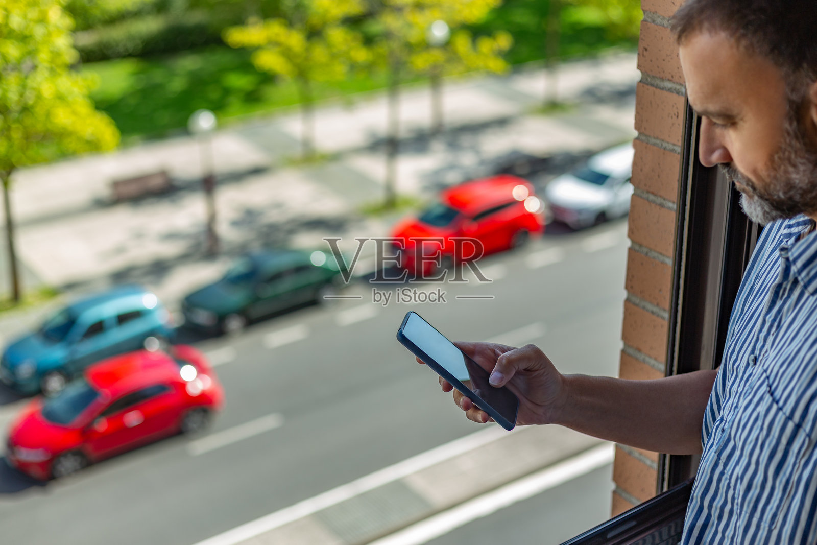 高角度视图,一位成熟男性在窗边看着手机,窗外是一条繁忙的街道。照片摄影图片