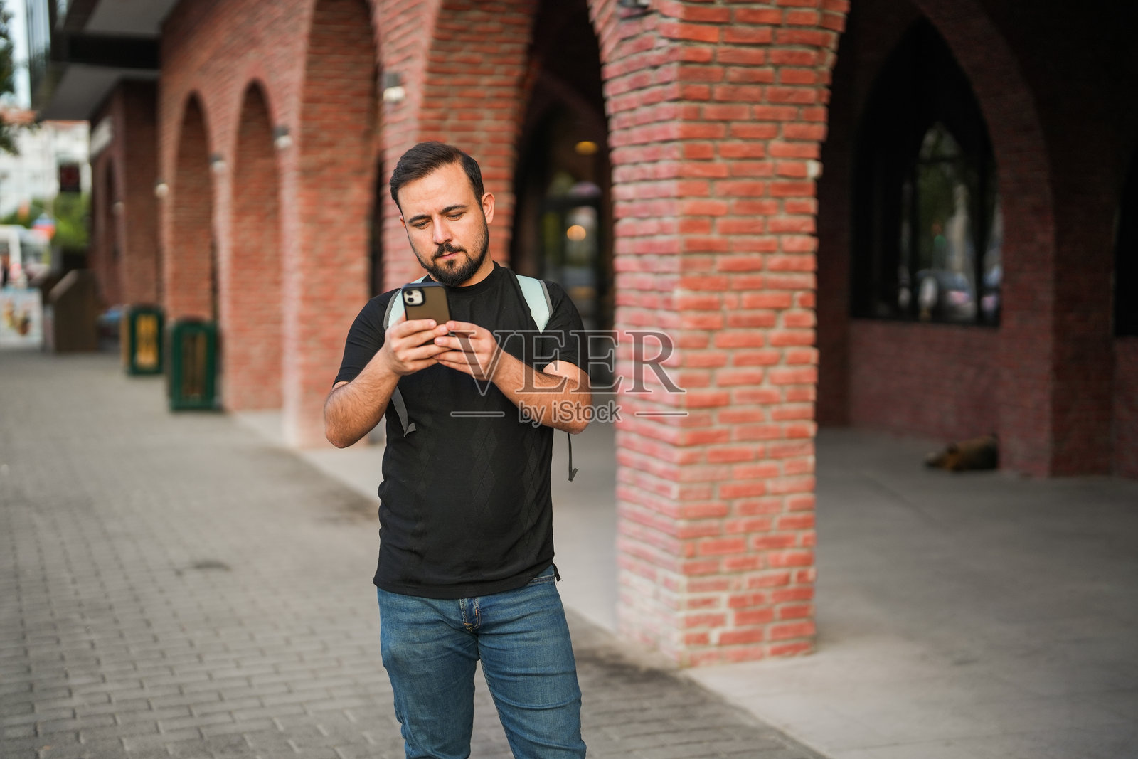 男子在市中心的街道上走着,低头看着手机。照片摄影图片