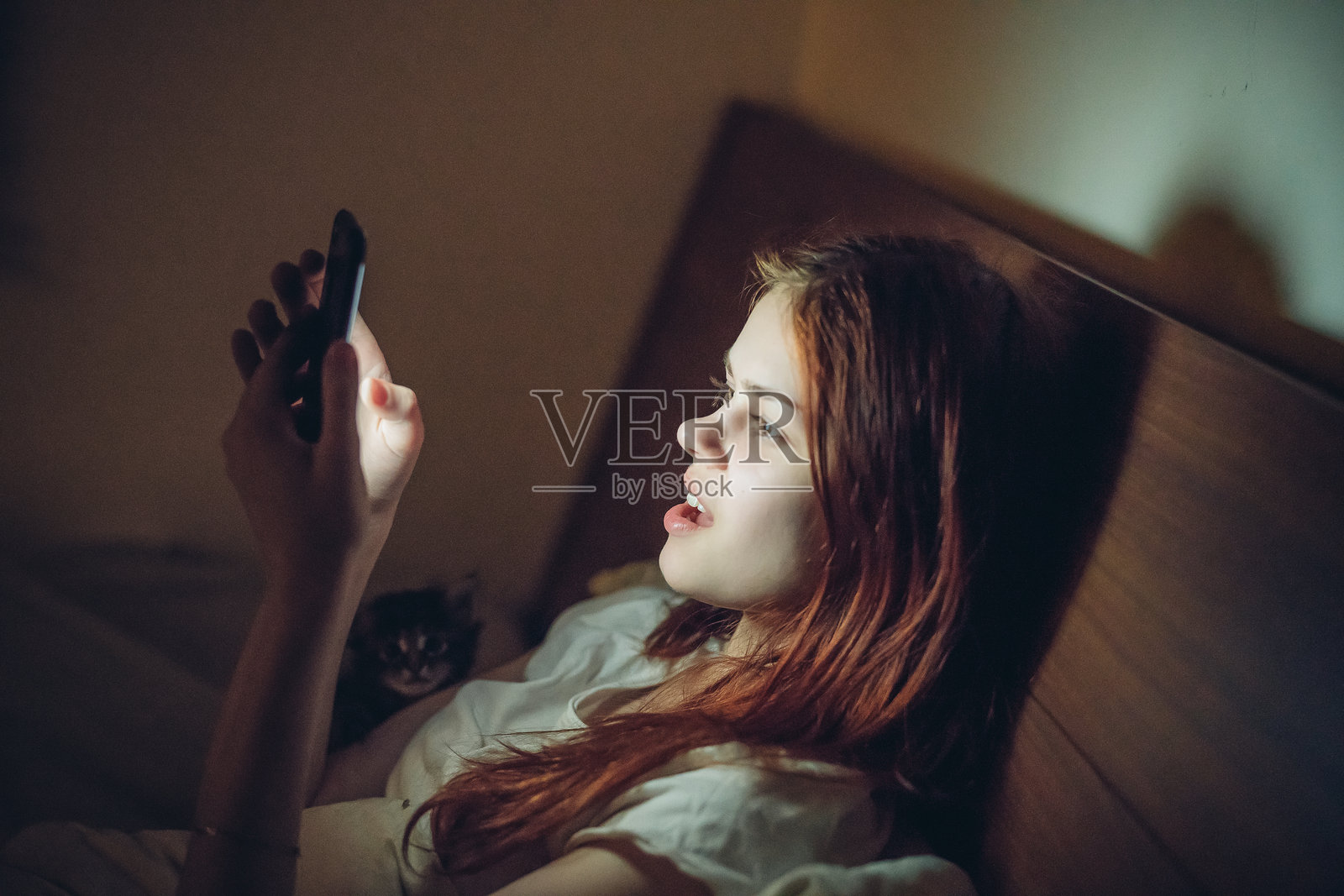 女人躺在床上,手里拿着手机在睡前观看新闻照片摄影图片