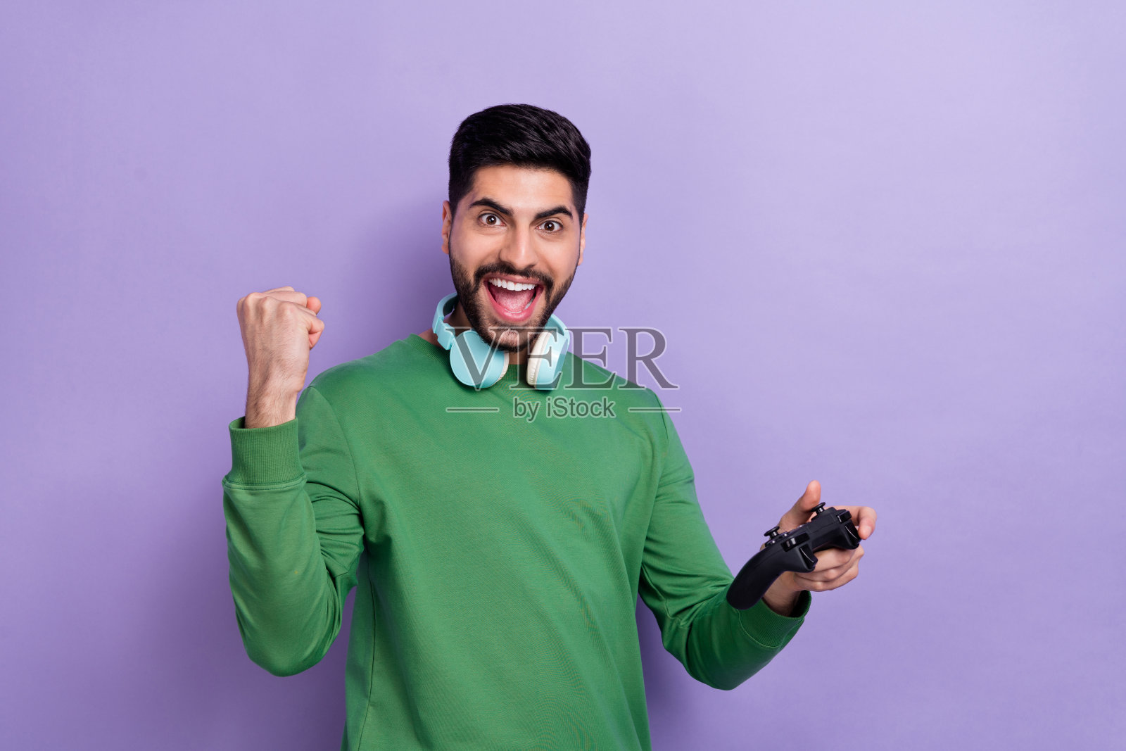 戴着耳机的乐观愉快的游戏玩家在紫色背景上大喊“耶!赢了!”照片摄影图片