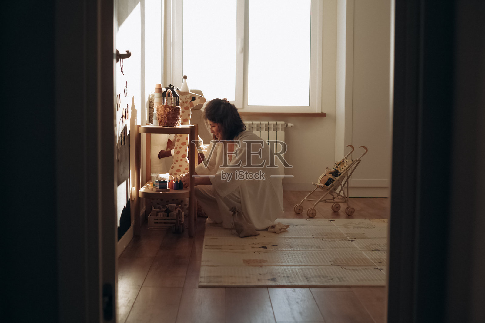 一位女性坐在地板上整理工艺用品,旁边有一张小桌子,房间光线明亮。阳光透过窗户洒入,营造出温暖的氛围,旁边有一个孩子在玩耍。照片摄影图片