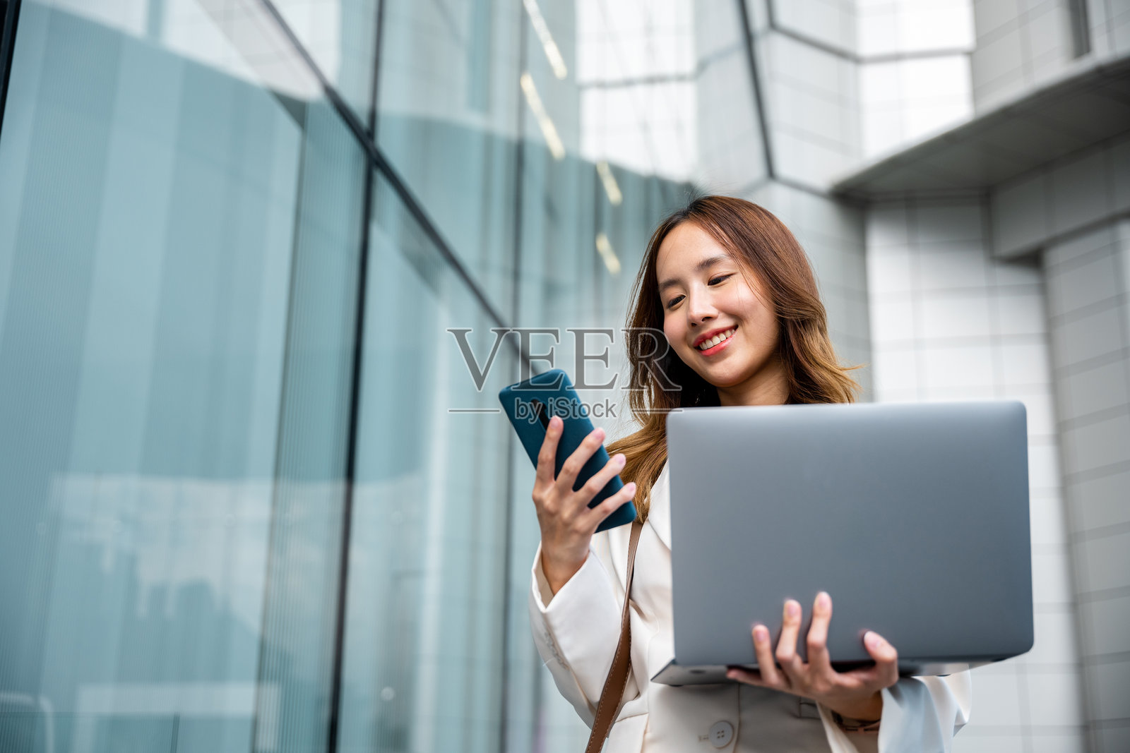 自信的女商人在城市中使用智能手机,旁边放着笔记本电脑照片摄影图片