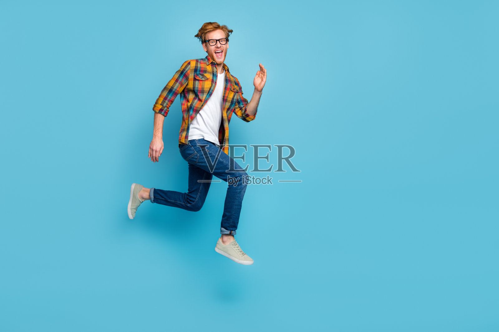 穿着格子衬衫和牛仔裤的时尚帅哥,红发,急于促销,兴奋地大喊“是的”,背景为蓝色。照片摄影图片