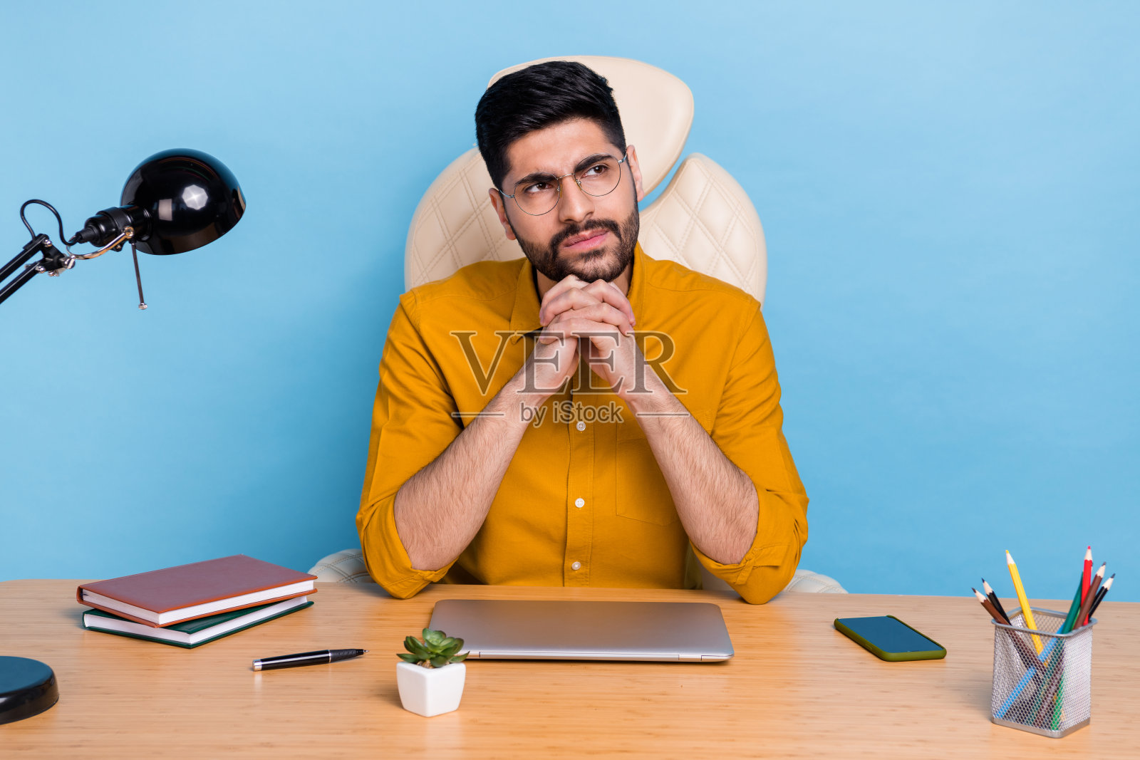 一个有思想的创意人士双臂托腮,凝视空旷的空间,沉思,背景为蓝色。照片摄影图片