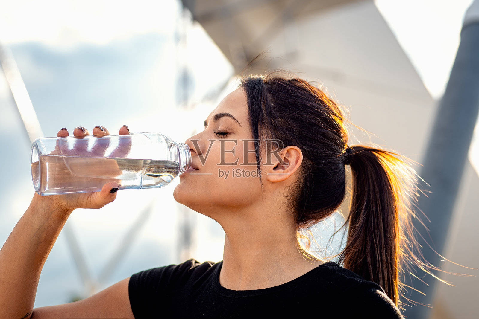 年轻女性穿着黑色运动服,跑步后休息并喝水。照片摄影图片