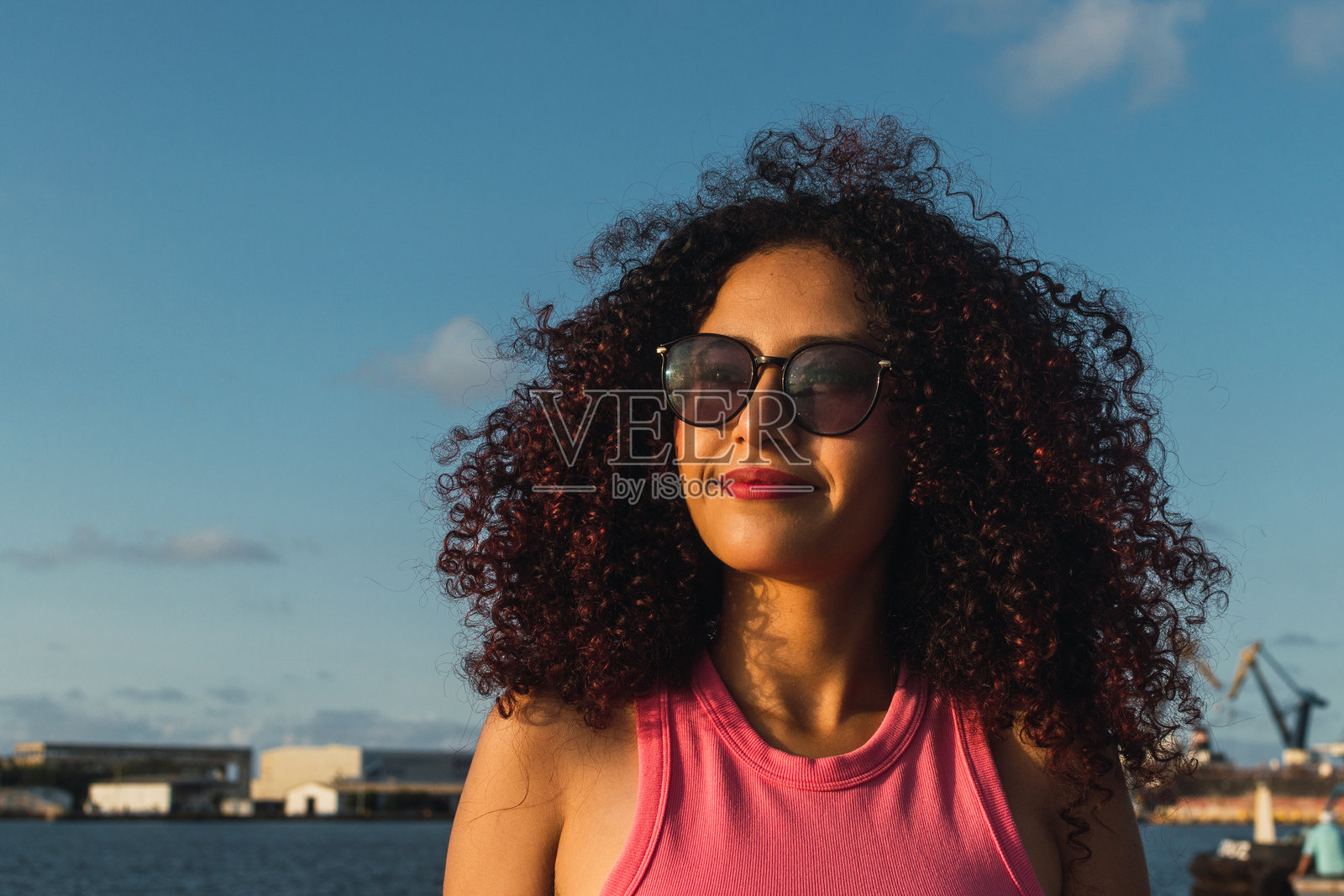 年轻的拉丁裔女性戴着太阳镜,在码头享受温暖的夏日。照片摄影图片