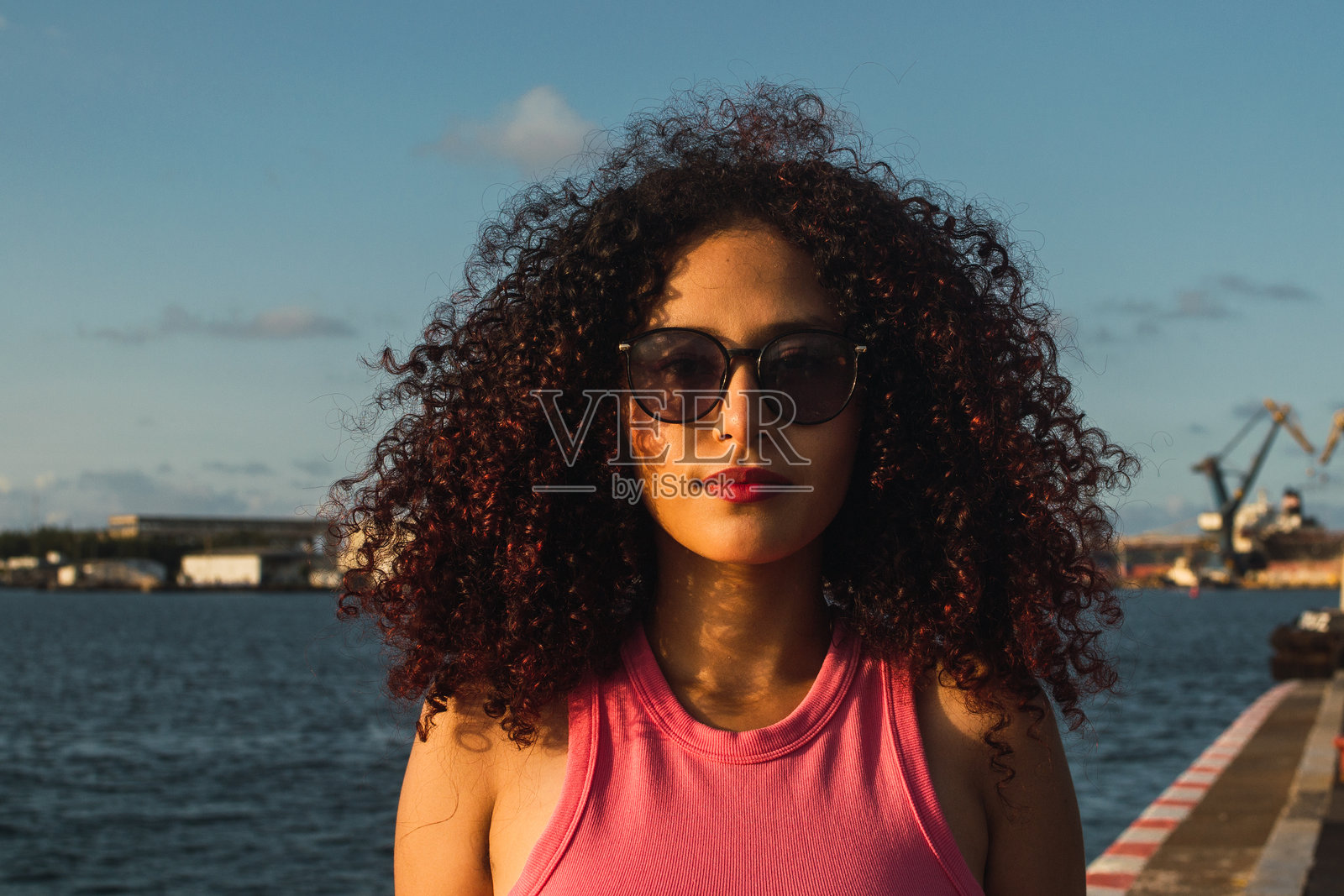 年轻女子戴着太阳镜,卷发在海边摆姿势照片摄影图片