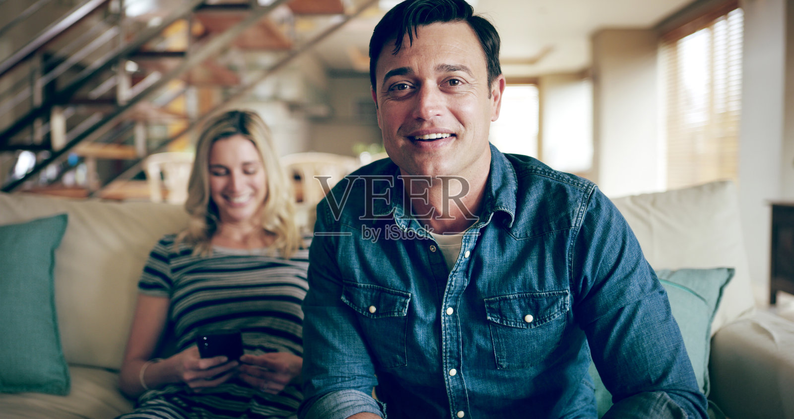 快乐的男人在家中沙发上放松,和女人一起观看电视,选择和观看节目。这个人在公寓的休息室沙发上微笑,浏览频道和电影。照片摄影图片