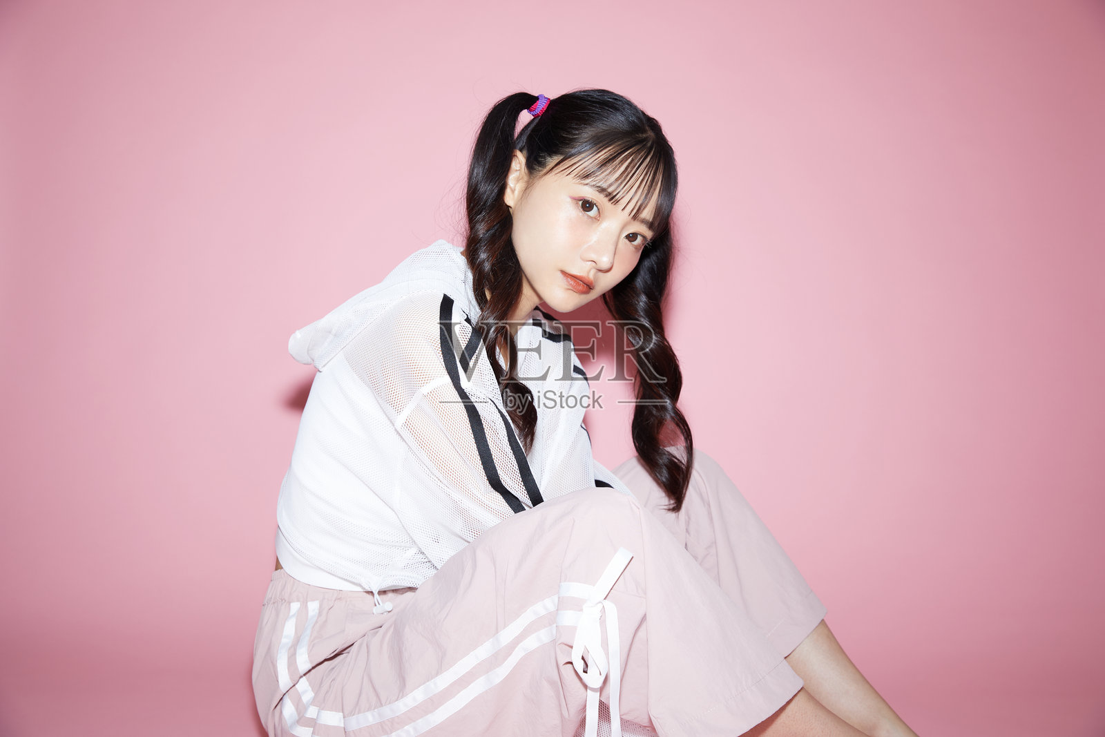 穿着运动服的年轻女性可爱的肖像,背景为粉色。照片摄影图片