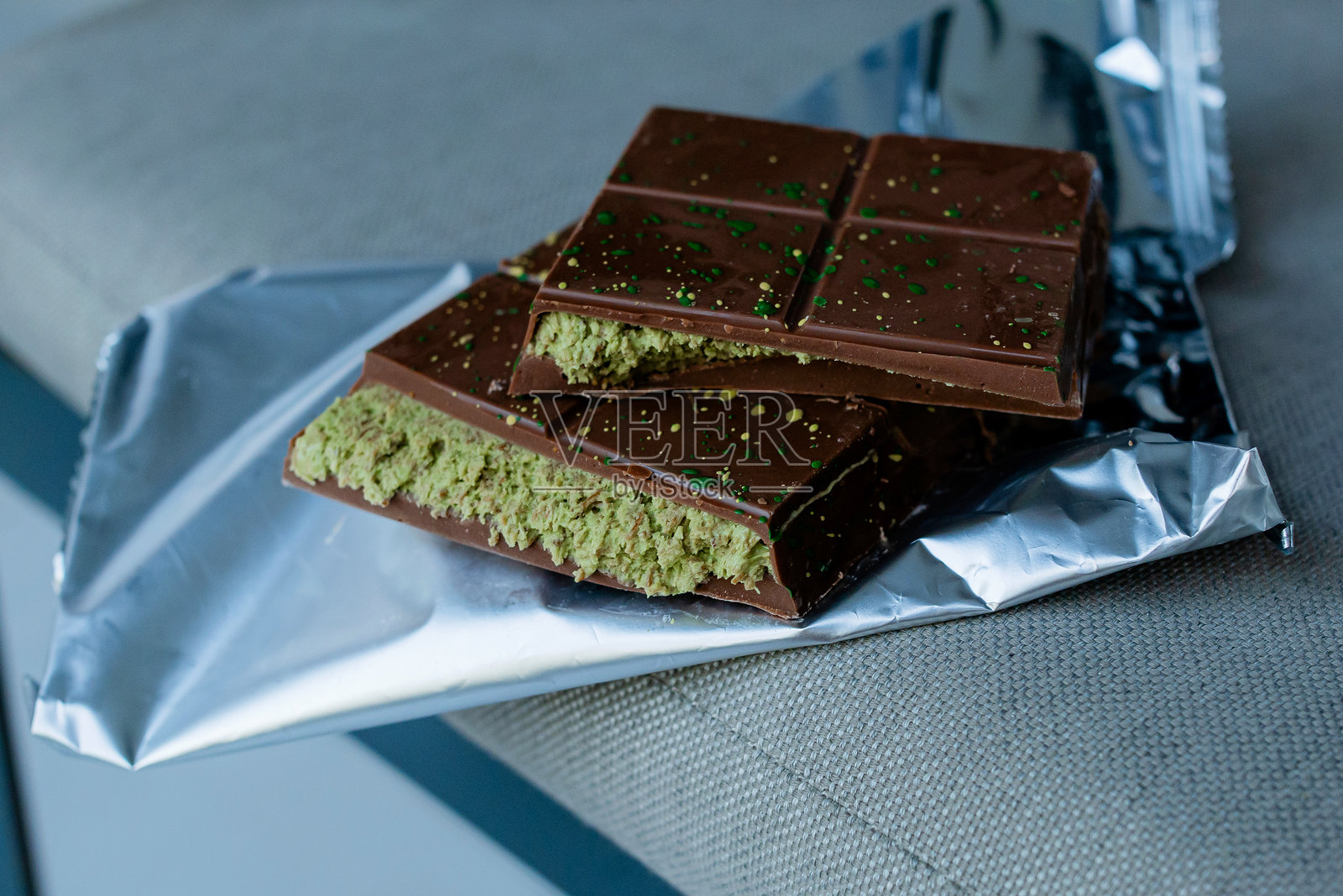 一块破碎的迪拜巧克力甜点,上面有绿色卡塔菲和开心果酱,奶油诱人地躺在铝箔包装上。照片摄影图片