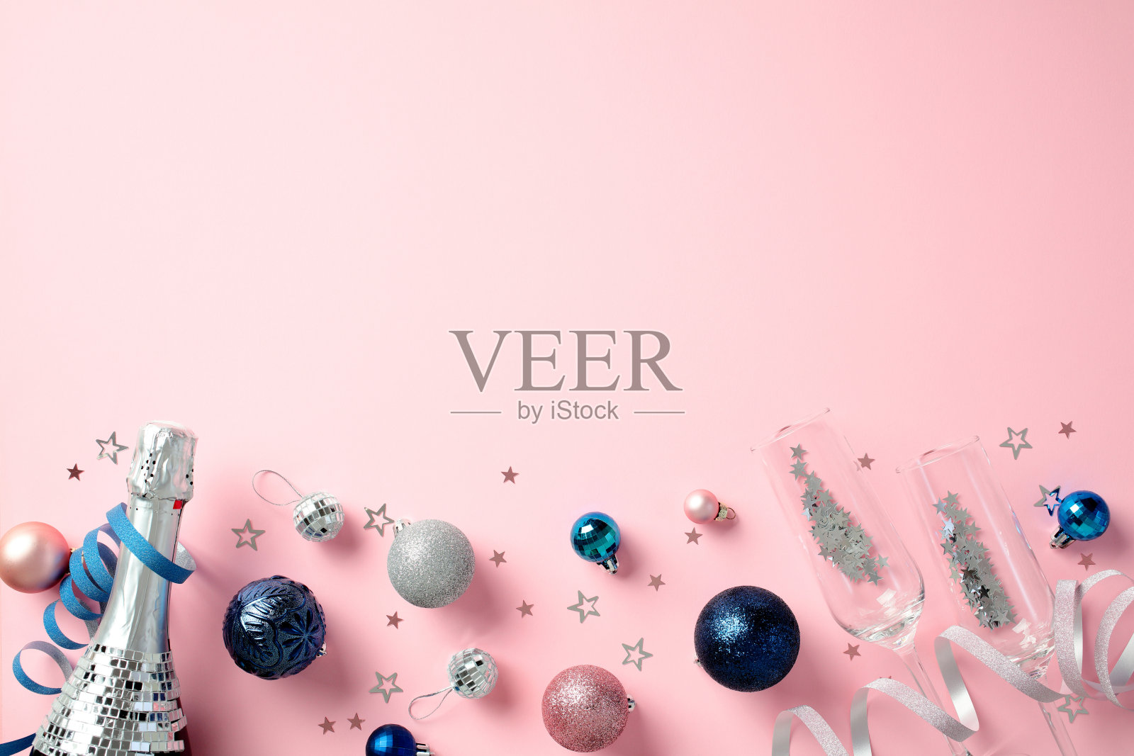 时尚的圣诞或新年平铺构图,包含香槟、酒杯,以及闪亮的蓝色、银色和粉色装饰,背景为柔和的粉色。照片摄影图片