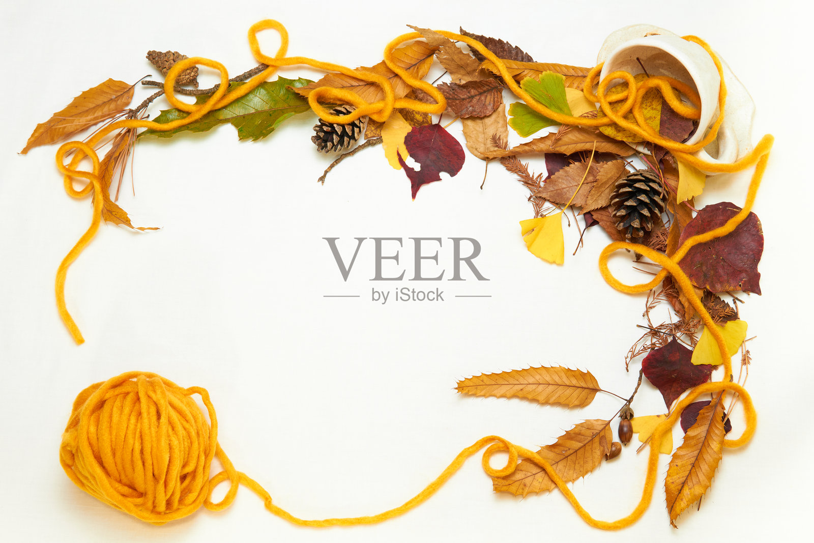 橙色毛线在由五彩缤纷的秋叶、橡果、松果和咖啡杯组成的框架上。照片摄影图片