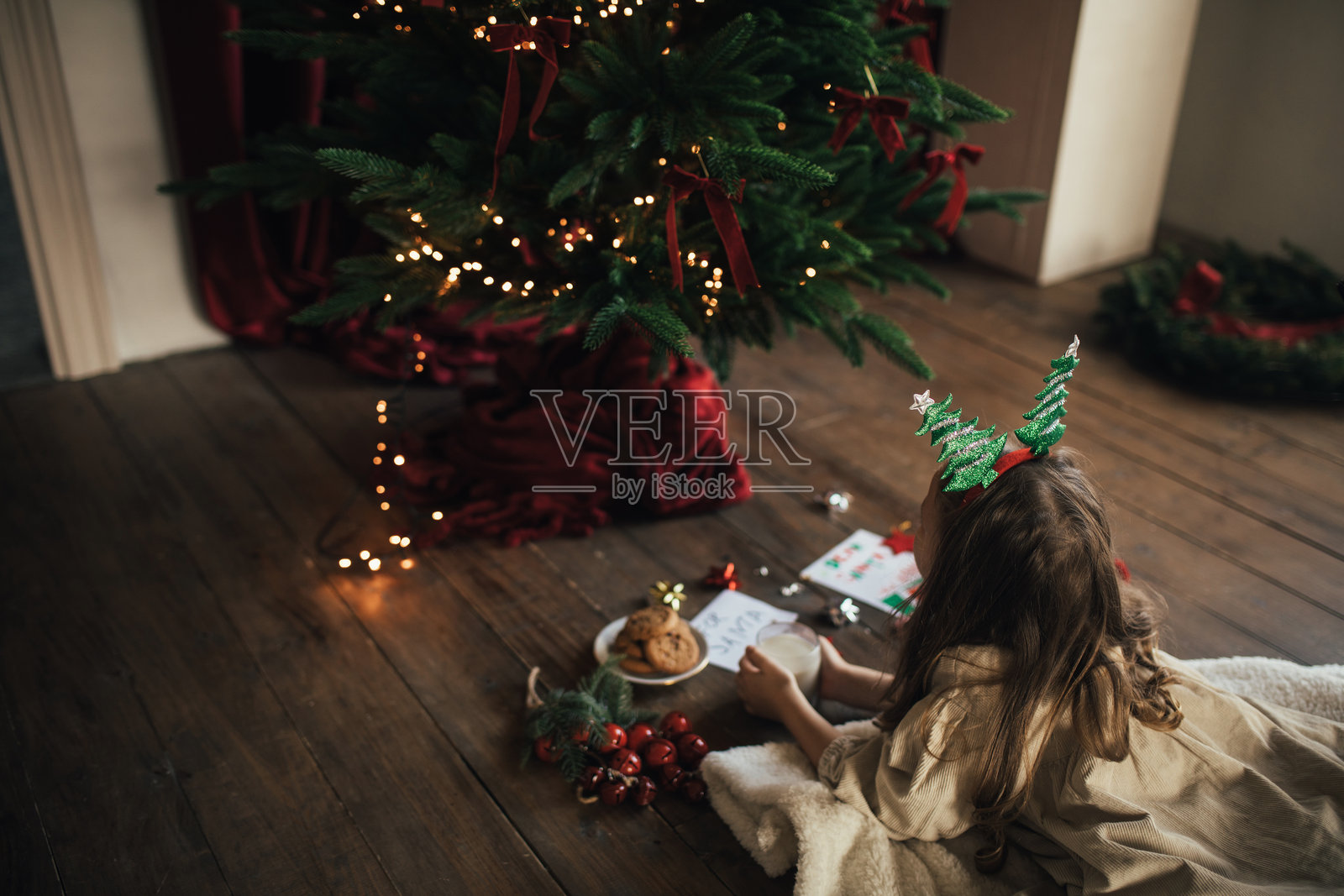 可爱的女孩在圣诞树下为圣诞老人准备牛奶和饼干。照片摄影图片