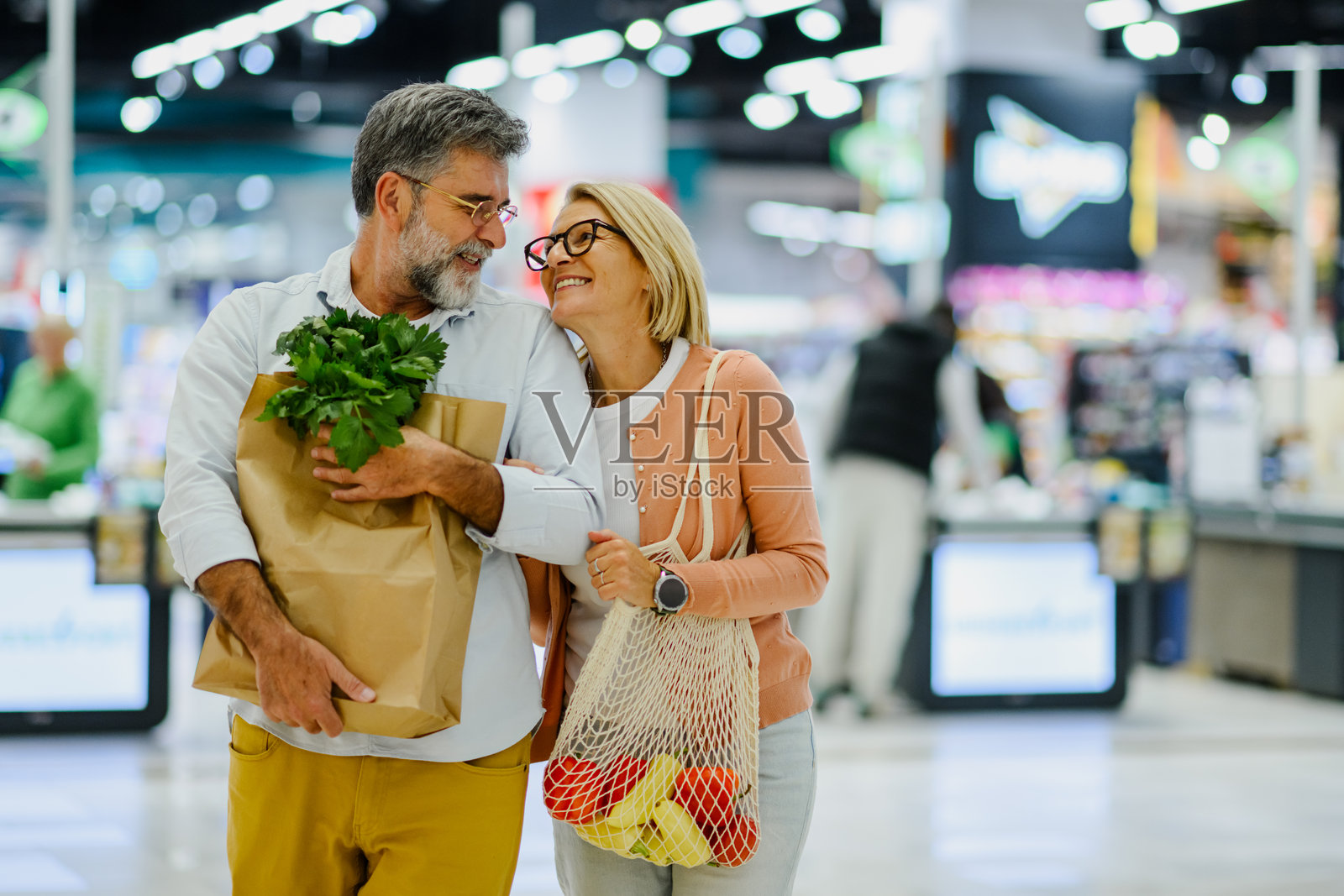 快乐的老年夫妇提着购物袋在超市里走着照片摄影图片