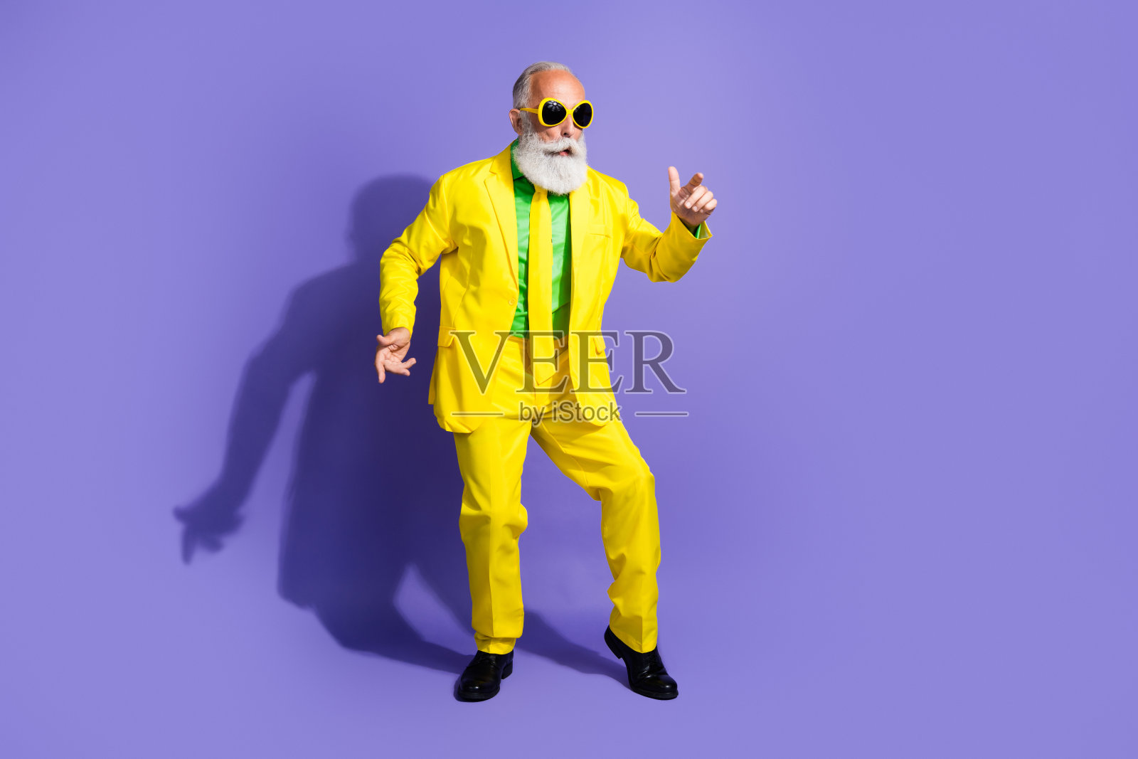 穿着时尚黄色西装、心情愉快的古怪乐观幽默的祖父,背景为紫色。照片摄影图片