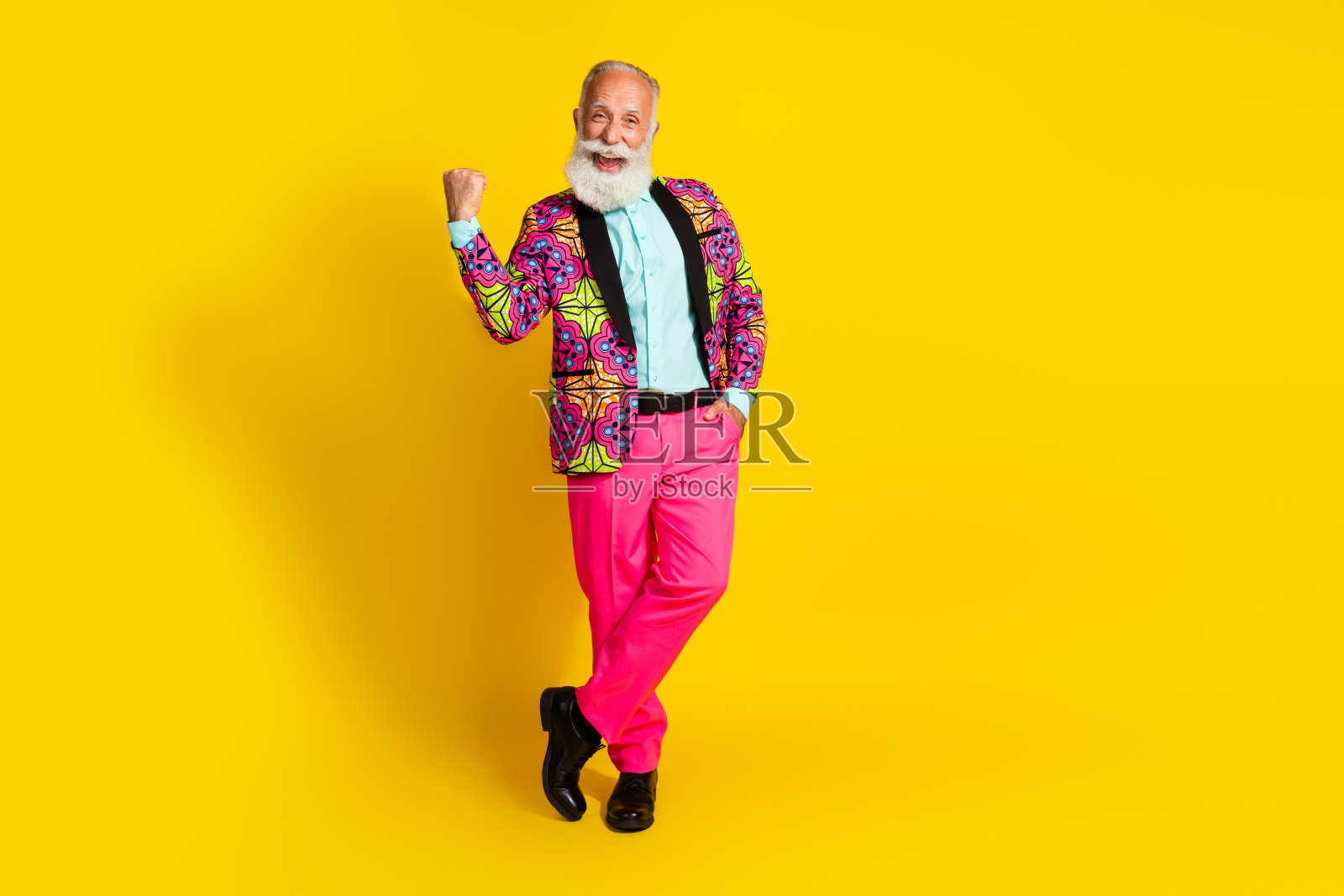 穿着西装的积极快乐的老年艺术家在黄色背景下举起拳头大喊“是的,胜利!”照片摄影图片
