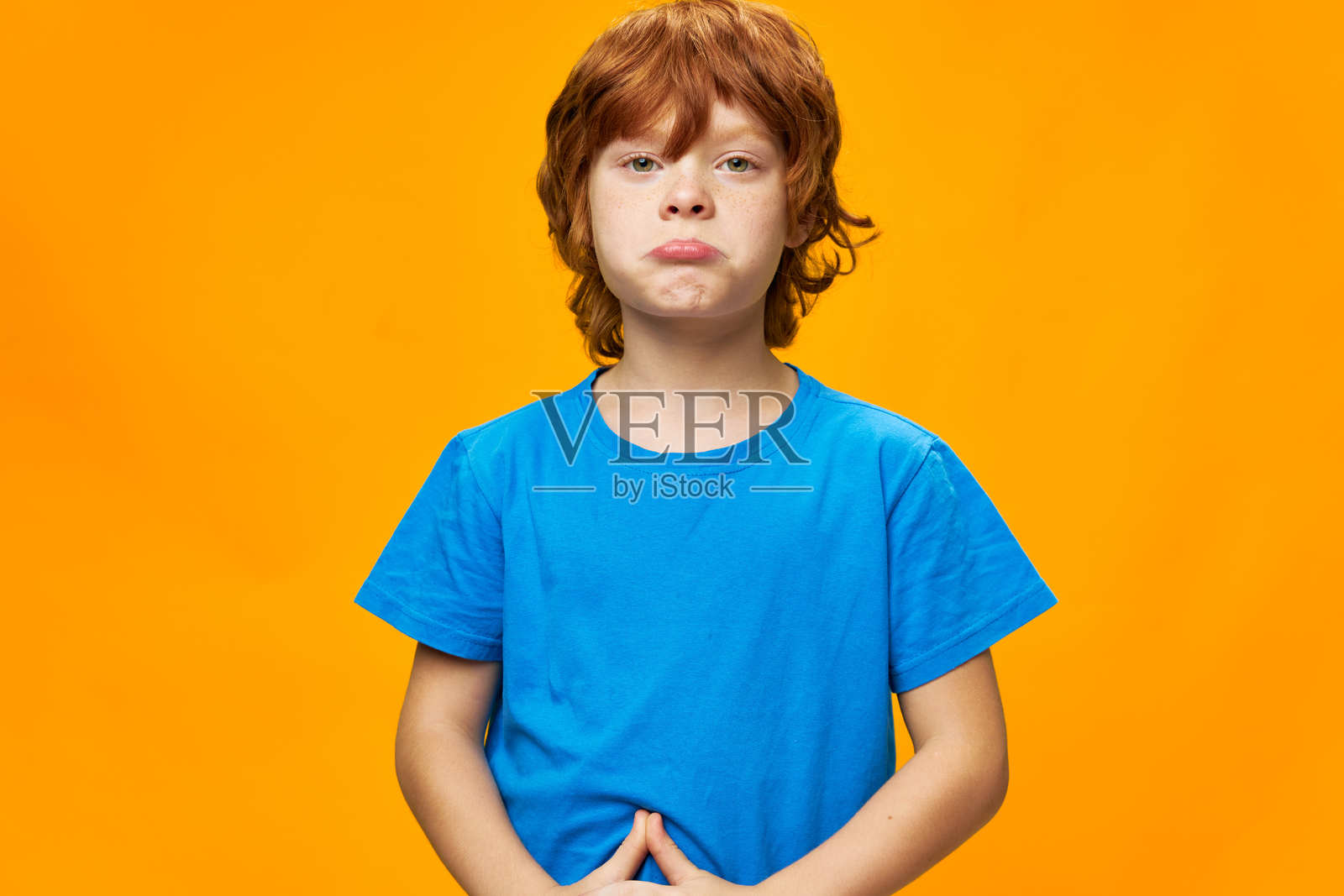 红发男孩 受伤的孩子撅着嘴穿着蓝色T恤 背景是黄色的照片摄影图片