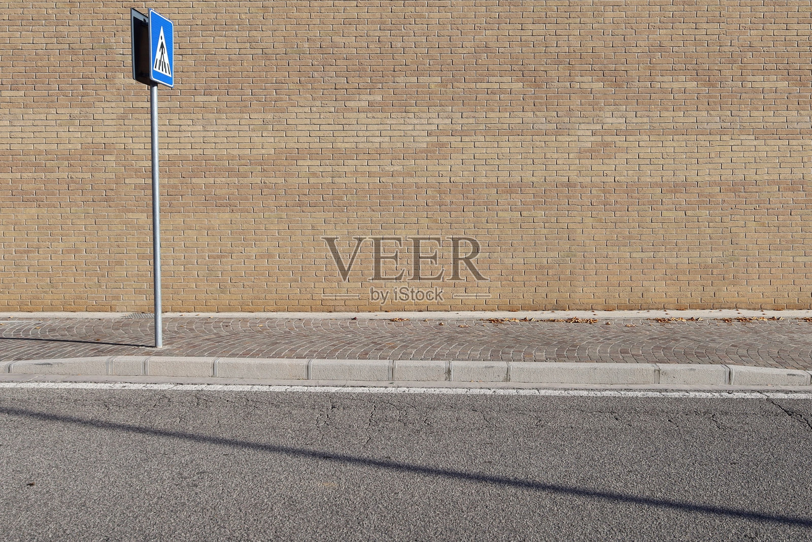 路边的黄色砖墙,左侧有一个人行横道标志。前面是人行道和沥青马路。照片摄影图片