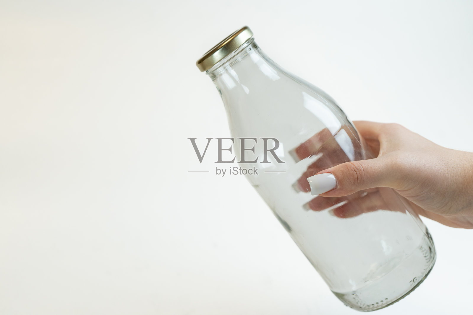 一只手伸出一瓶透明的牛奶。照片摄影图片