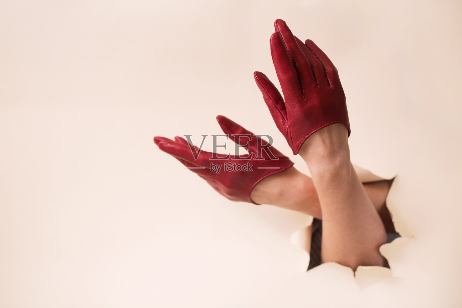 两只穿着酒红色皮手套的女性手伸入米色纸张的孔中照片摄影图片