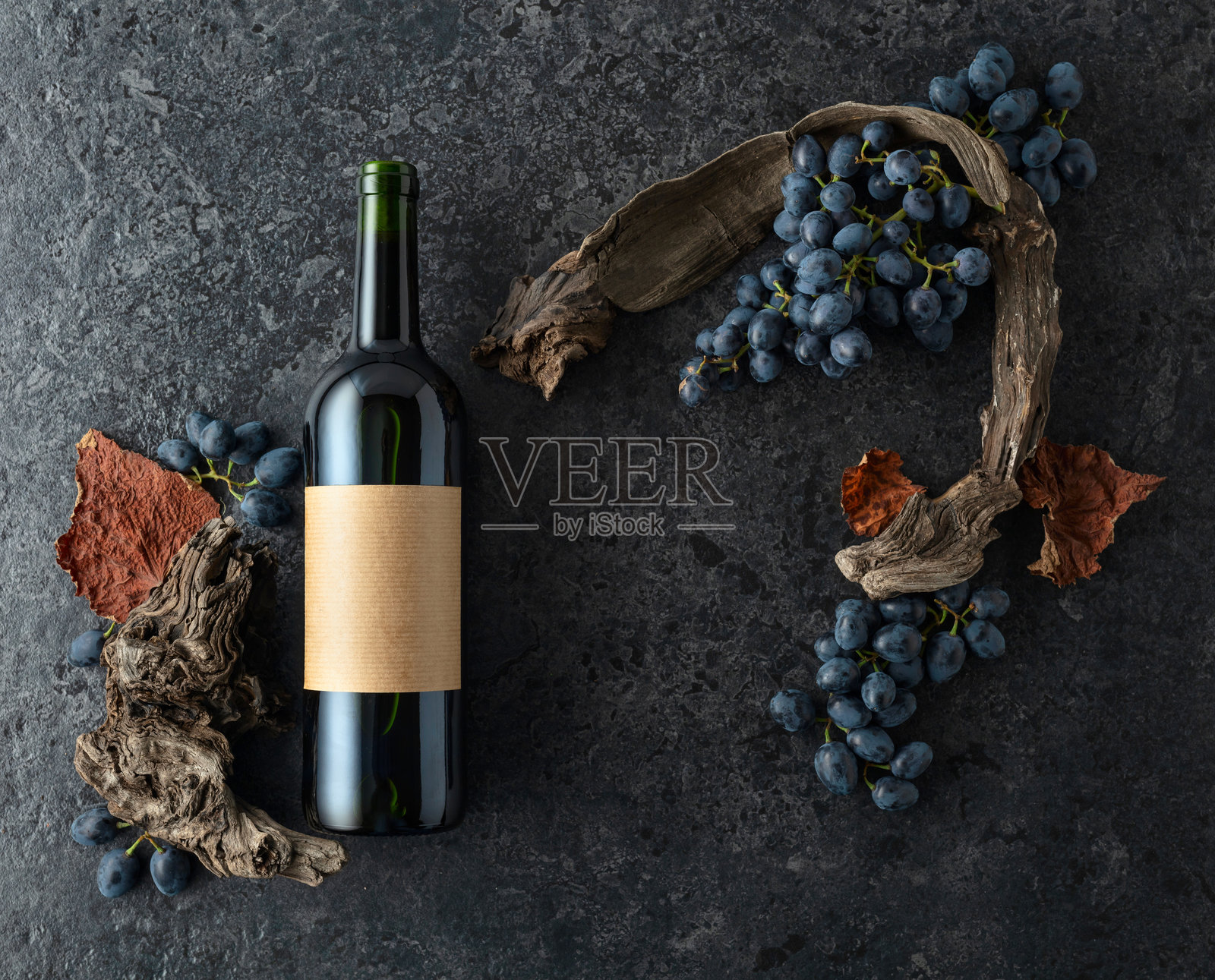 红酒瓶、蓝色葡萄和古老的藤蔓在黑色石头背景上。照片摄影图片
