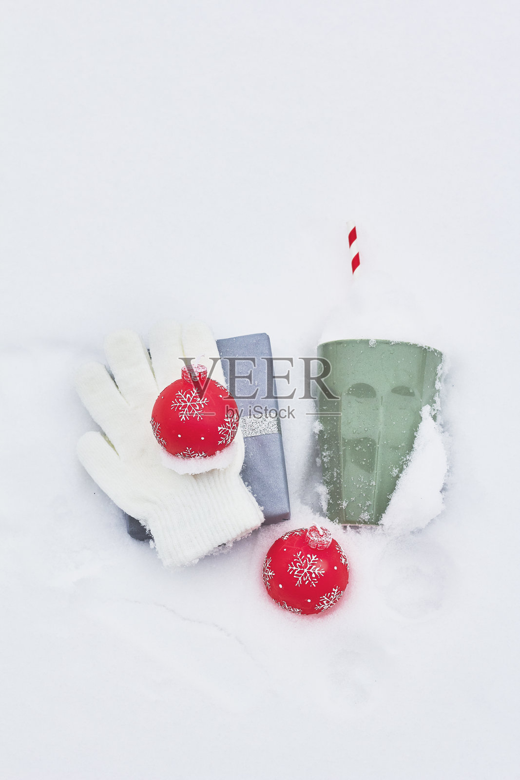 红色装饰品、绿色杯子、白色手套和银色礼品盒在雪地上的平铺排列照片摄影图片