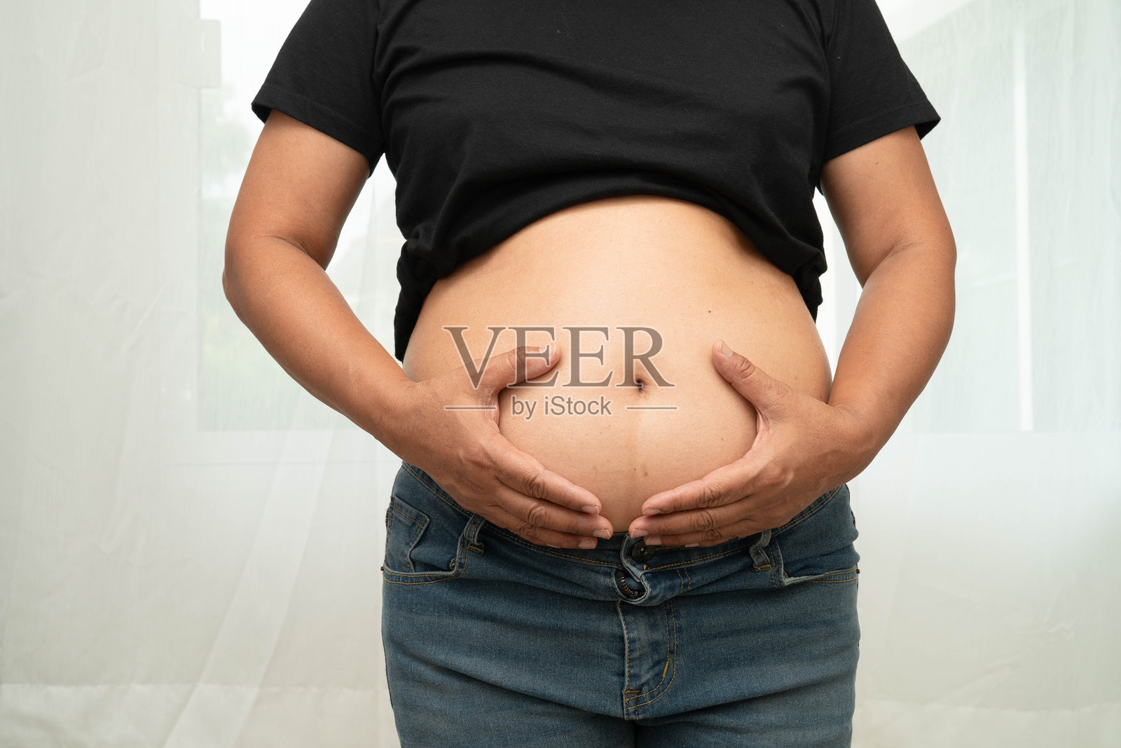 超重的亚洲女性用手捏着肥胖的大肚子,体现出超重和肥胖。照片摄影图片