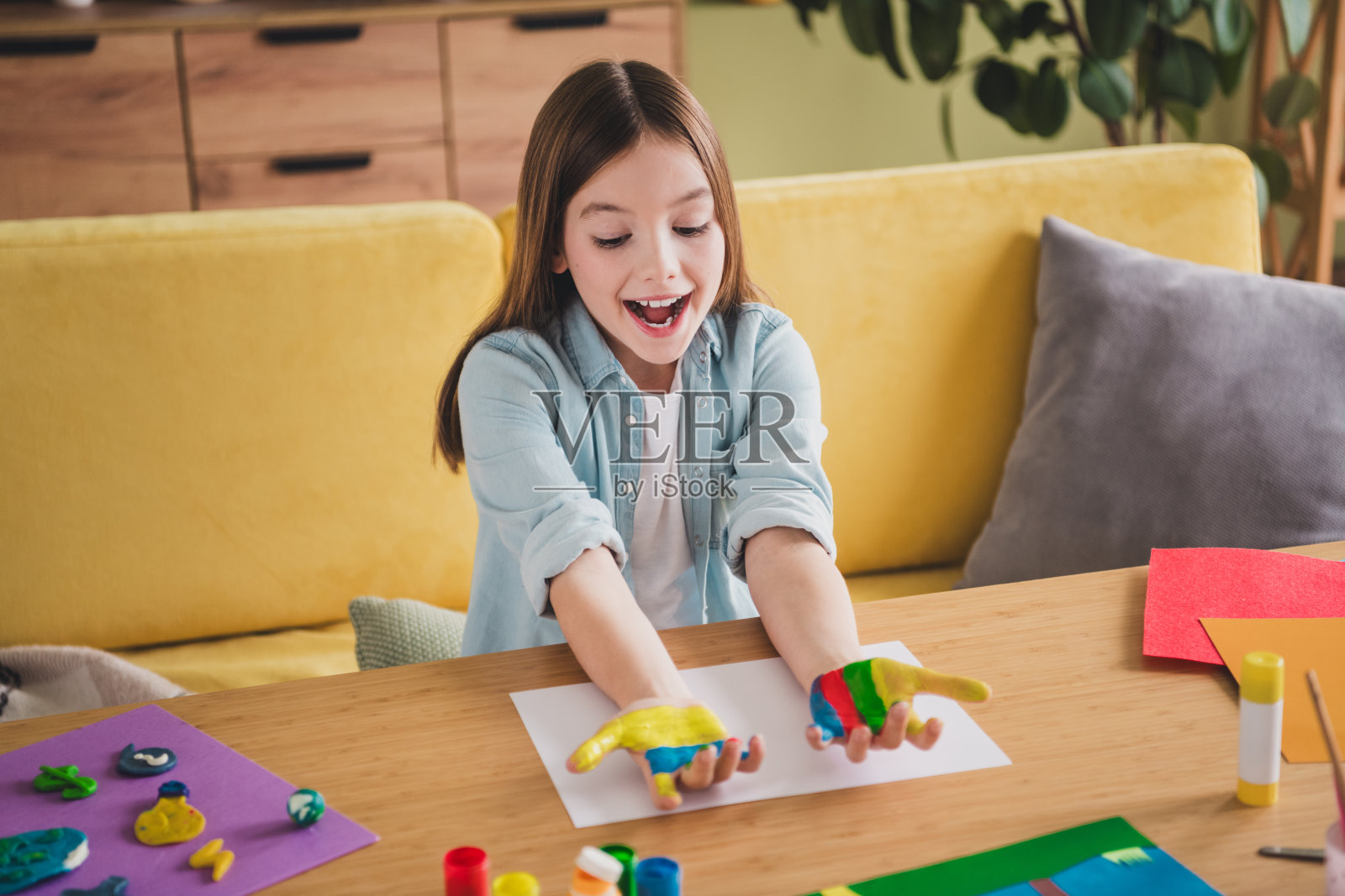 可爱的年轻女孩在家中享受创意艺术时光,穿着休闲的牛仔衬衫,开心而放松地使用五颜六色的颜料。照片摄影图片