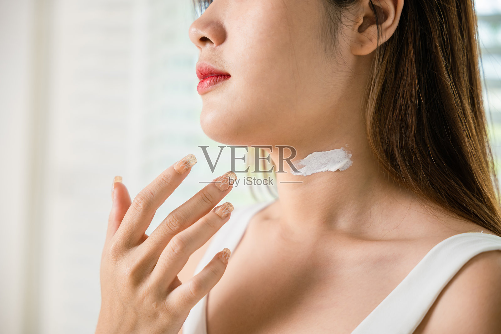 亚洲美丽年轻女性在家中涂抹颈部护肤霜照片摄影图片