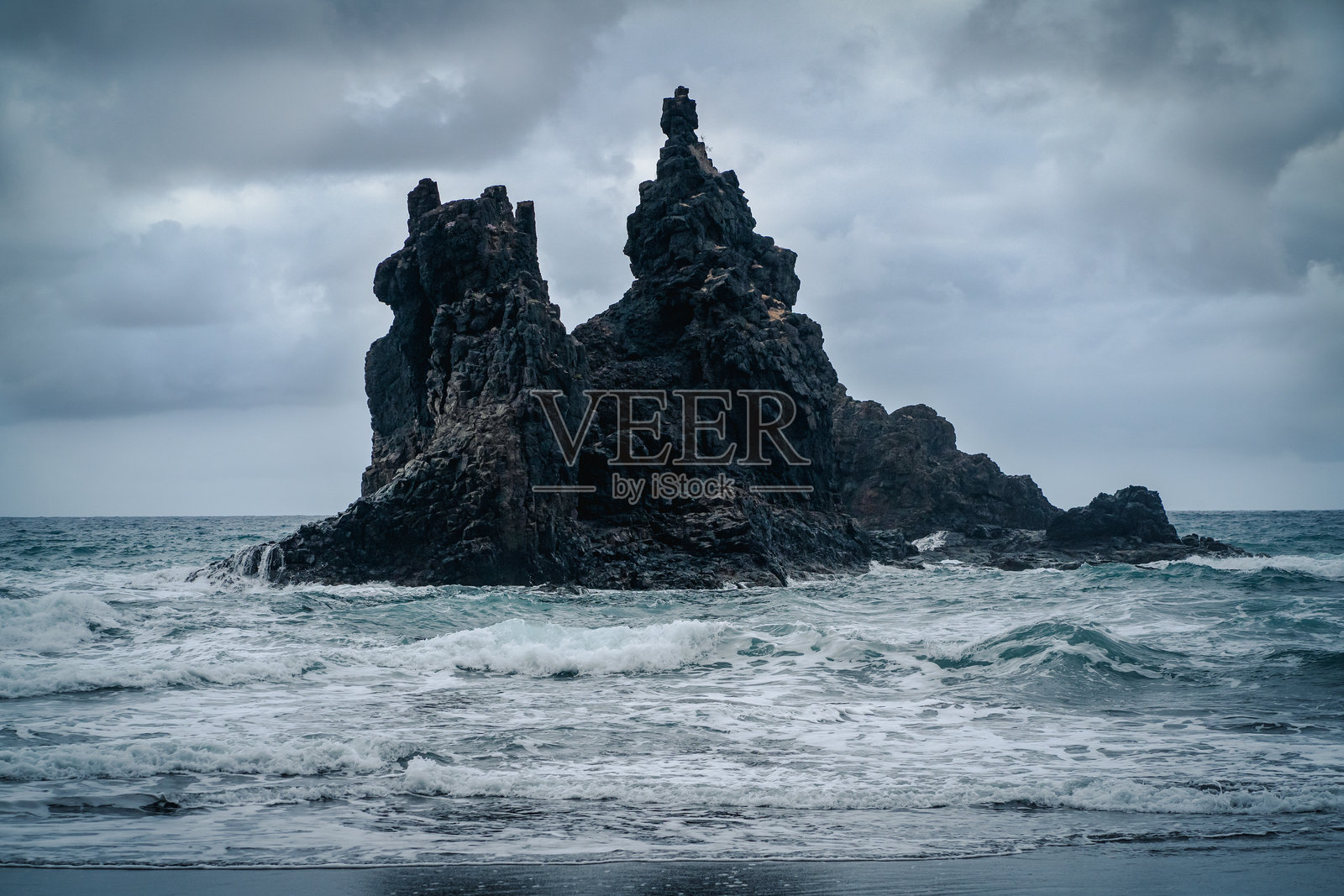 在阴云密布的天气中,黑暗的岩石矗立在波涛汹涌的海洋中。照片摄影图片