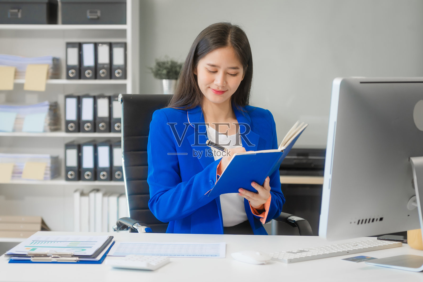 一位年轻的亚洲女性在办公室的桌子上工作,使用笔记本电脑、文件和财务图表来管理时间。她专注于在多个领域提供咨询服务,从战略到人力资源和法律。照片摄影图片