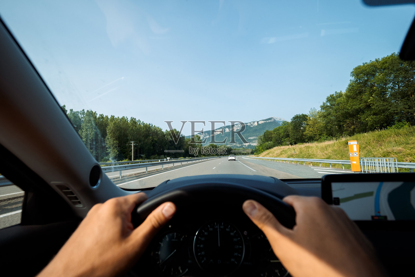 司机在高速公路上驾驶,手握方向盘,身旁是山脉。照片摄影图片