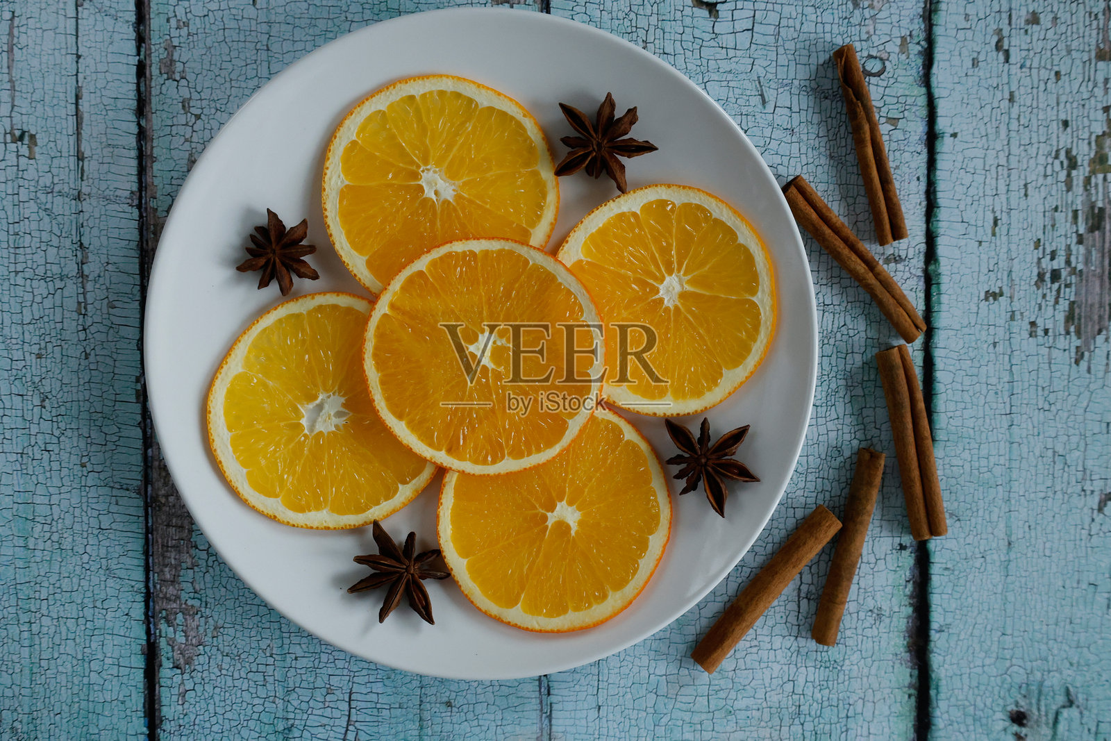 一只白色盘子里盛满鲜艳的橙子片,周围点缀着八角和肉桂棒。照片摄影图片