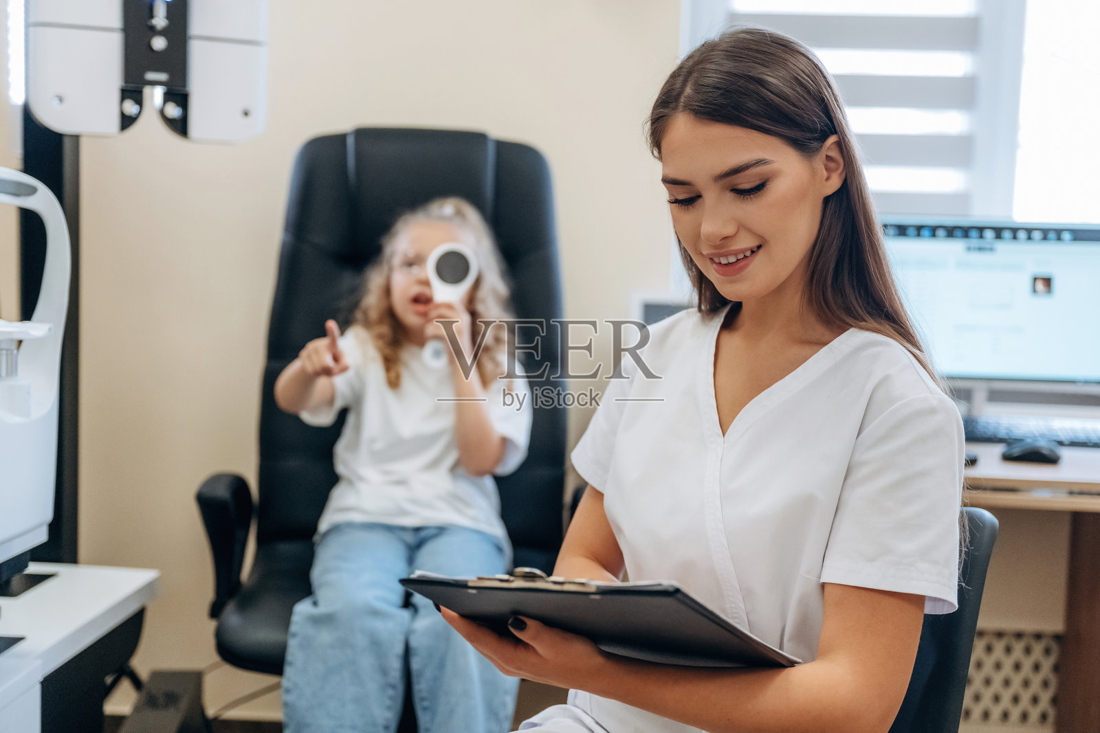 女性手持记事本。小女孩在眼科诊所与医生在一起。照片摄影图片