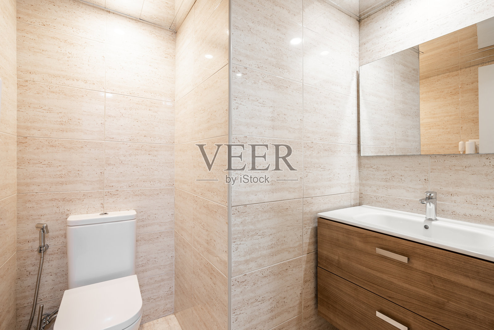 简单的浴室,配有白色马桶、木质家具和米色瓷砖。现代翻新的公寓内部。照片摄影图片