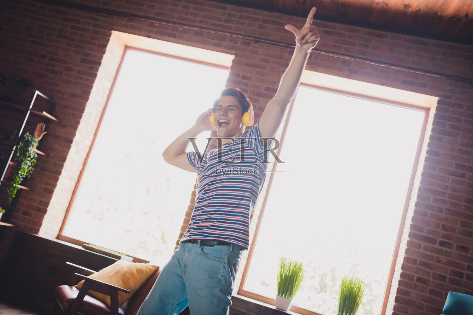 年轻男子在明亮舒适的客厅里,愉快地戴着耳机跳舞,享受音乐的快乐午后。照片摄影图片