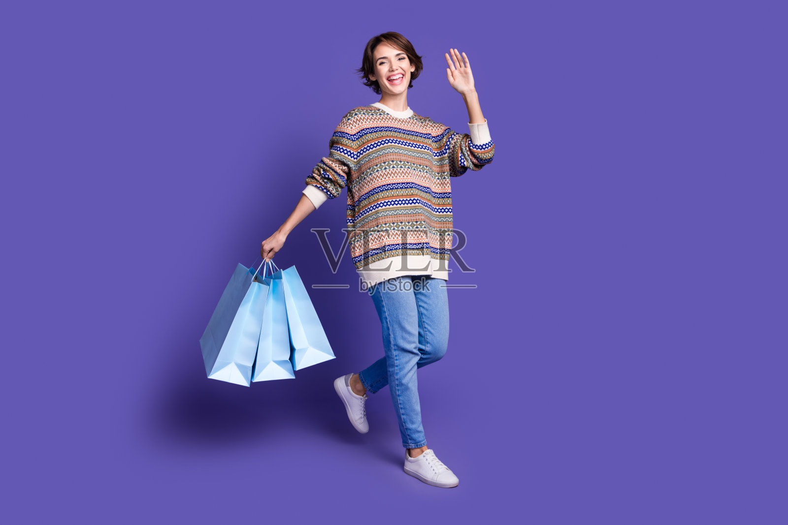 穿着时尚印花衣服的快乐女性,手提包裹,背景为紫色。照片摄影图片