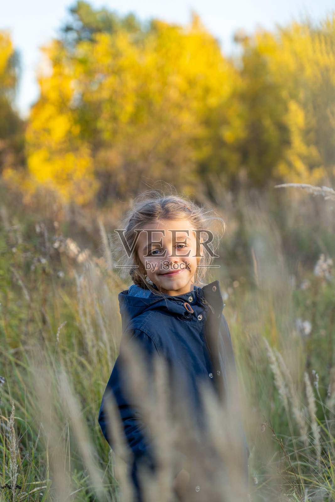 微笑的女孩站在公园里看着镜头。帅气的孩子展现时尚的城市年轻生活方式,站在模糊的秋季背景前转身面对镜头。照片摄影图片