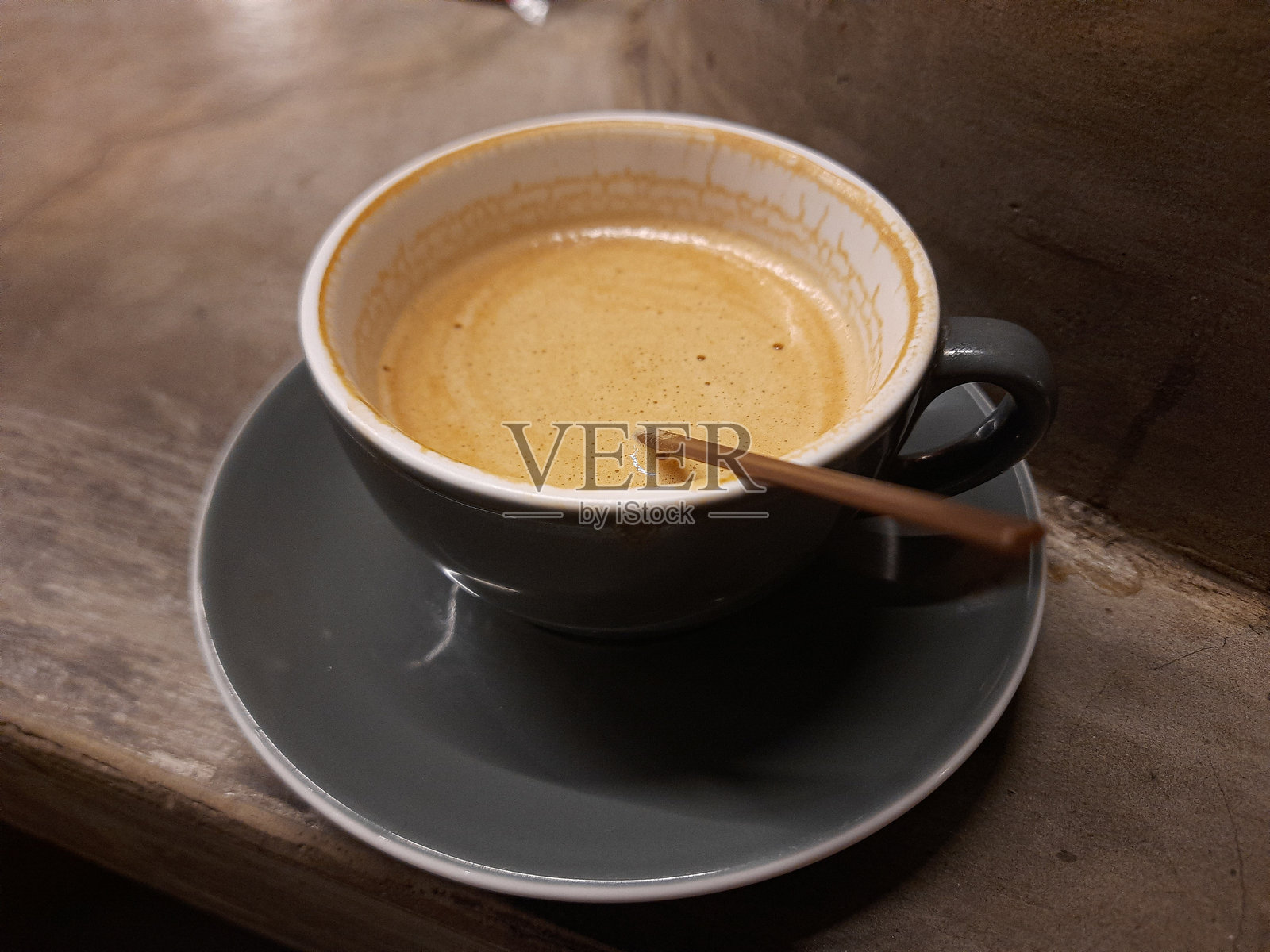 热拿铁咖啡在灰色陶瓷杯和碟子上,配有咖啡搅拌棒照片摄影图片