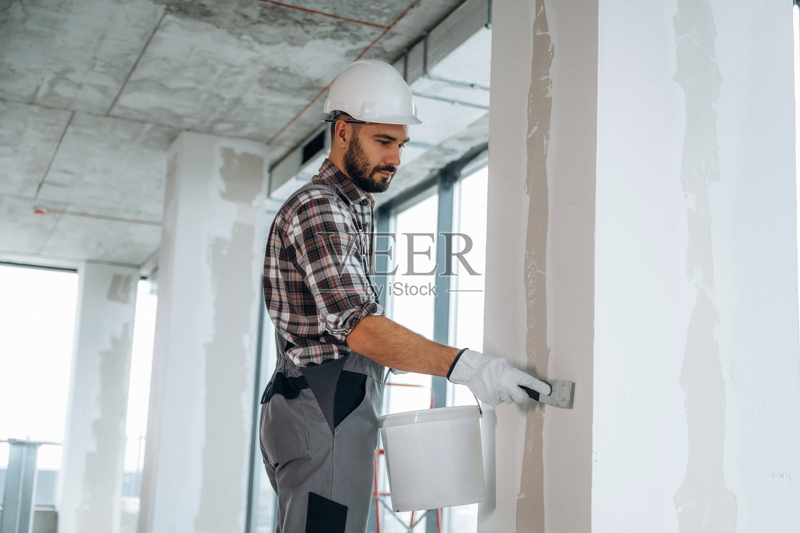 在粉刷墙壁。一名男子正在翻新一个未完成的房间。照片摄影图片