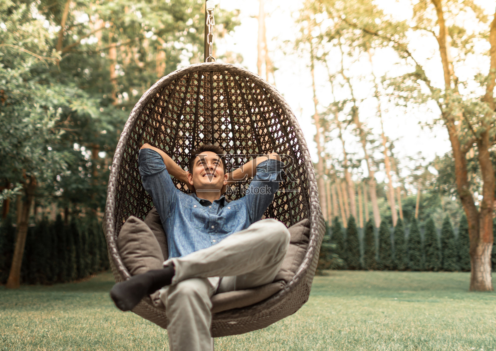 快乐的年轻男子微笑着坐在户外的院子里,享受周末的放松时光。照片摄影图片