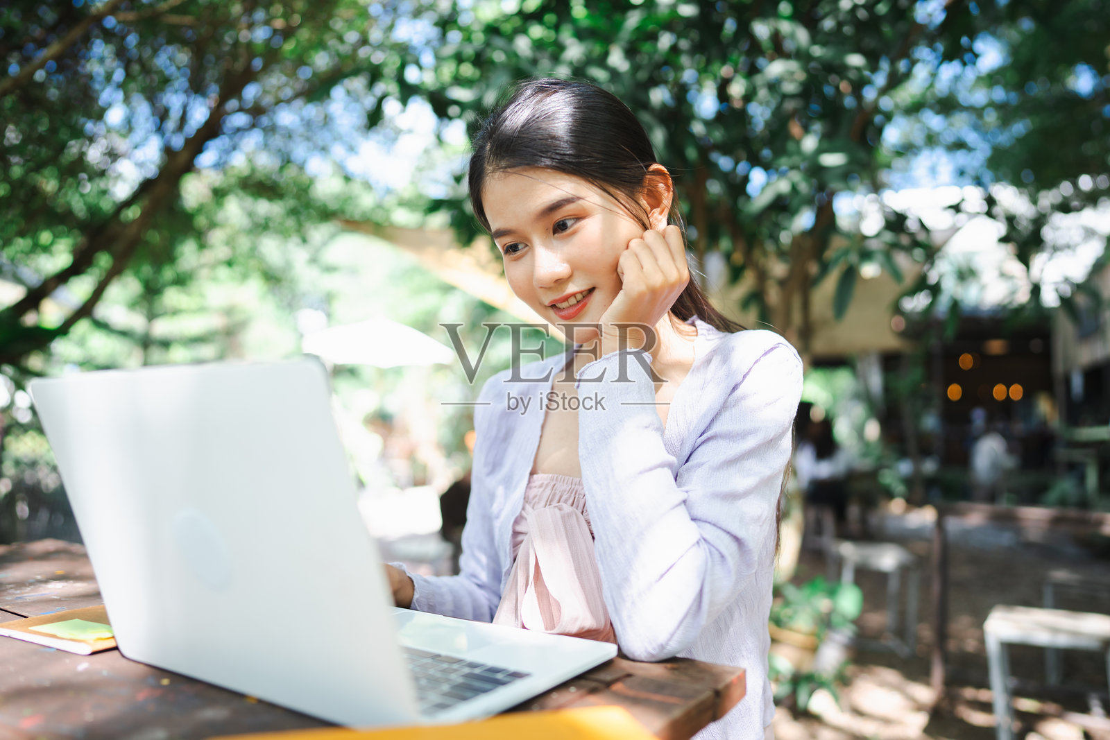 美丽自信的亚洲年轻女性在户外生态咖啡馆用笔记本电脑工作,手指在键盘上敲打。数字游牧者在大自然中远程工作。照片摄影图片