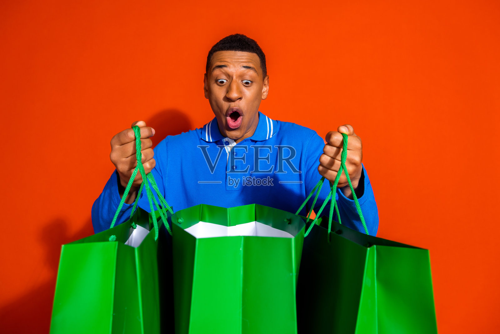 兴奋的年轻人手持购物袋,背景为鲜艳的橙色照片摄影图片